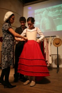 Kitty is tying the Spanish Farthingale to brass-tipped cords hanging from the waistline of the corset. This supports the Farthingale so it doesn't slip down.